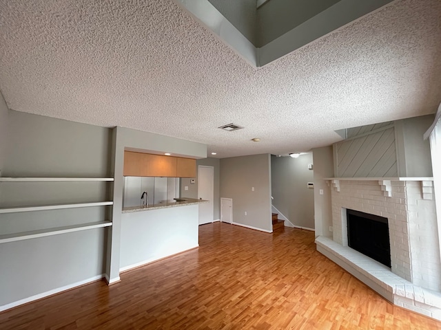 unfurnished living room with a textured ceiling, sink, a fireplace, and hardwood / wood-style floors