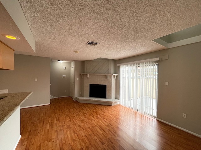 unfurnished living room featuring a textured ceiling, a brick fireplace, and hardwood / wood-style floors