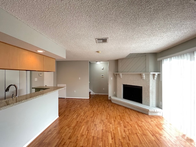 unfurnished living room with sink, a fireplace, a textured ceiling, and light hardwood / wood-style flooring