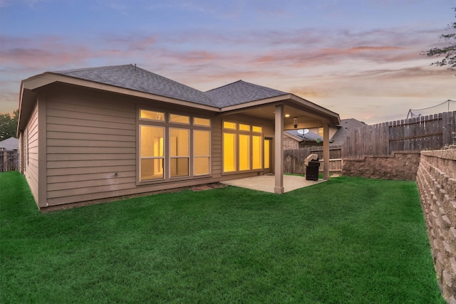 back house at dusk with a patio area and a yard