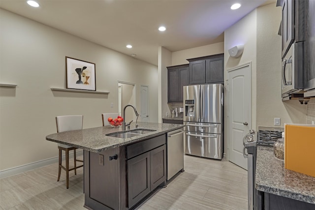 kitchen with light tile patterned flooring, dark stone countertops, appliances with stainless steel finishes, a kitchen breakfast bar, and a kitchen island with sink