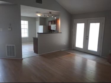 unfurnished living room with vaulted ceiling, wood-type flooring, rail lighting, and french doors