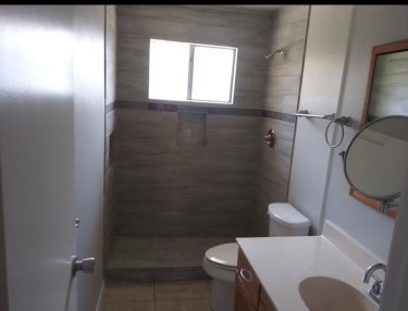 bathroom featuring a shower, vanity, tile patterned flooring, and toilet