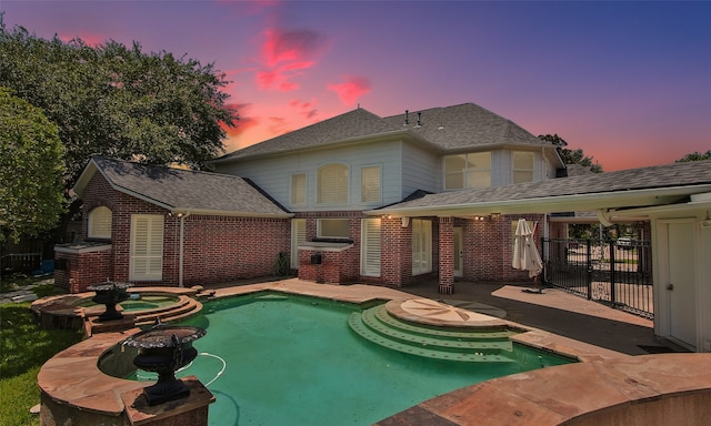 pool at dusk with a patio and an in ground hot tub