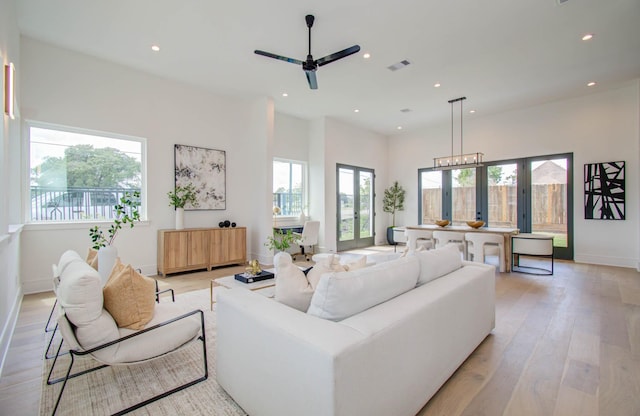 living room featuring french doors, ceiling fan with notable chandelier, and light hardwood / wood-style flooring