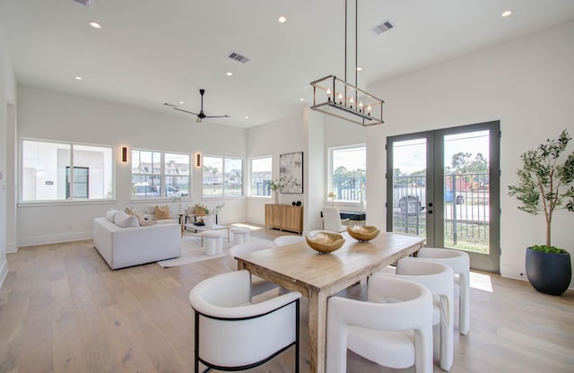 dining room featuring ceiling fan with notable chandelier, light hardwood / wood-style flooring, a wealth of natural light, and french doors