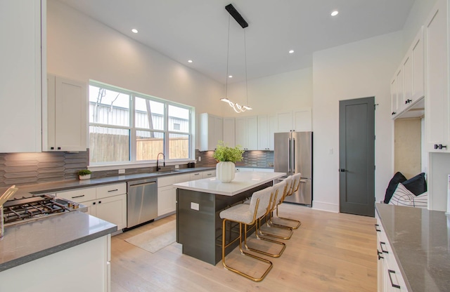 kitchen with a breakfast bar, stainless steel appliances, pendant lighting, white cabinets, and a center island