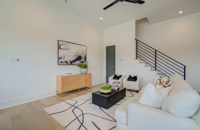 living room with ceiling fan, light hardwood / wood-style flooring, and a high ceiling