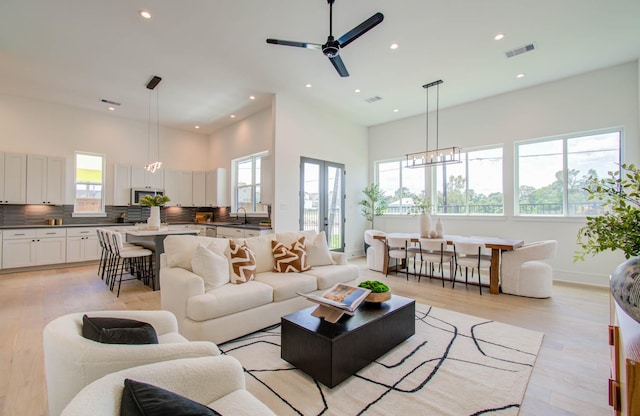 living room with ceiling fan with notable chandelier, light wood-type flooring, and sink