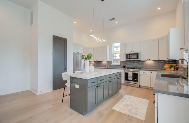 kitchen with stainless steel appliances, sink, a high ceiling, gray cabinets, and a kitchen island