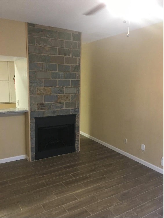 unfurnished living room featuring ceiling fan, a stone fireplace, and dark wood-type flooring