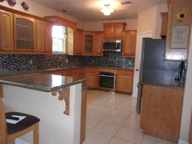 kitchen featuring light tile patterned flooring, tasteful backsplash, a breakfast bar area, appliances with stainless steel finishes, and kitchen peninsula