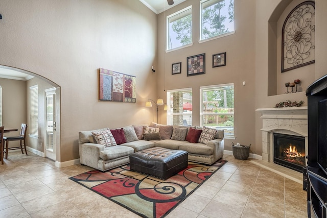 tiled living room with a fireplace, crown molding, a wealth of natural light, and a high ceiling