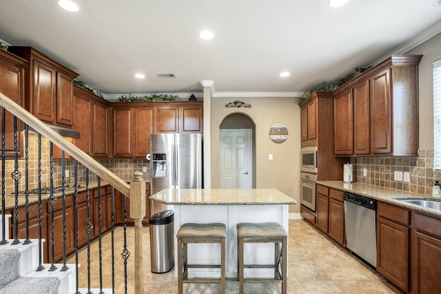 kitchen featuring a breakfast bar, a center island, ornamental molding, appliances with stainless steel finishes, and backsplash