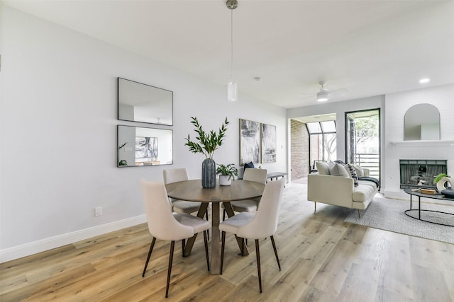 dining space featuring a fireplace, light wood-type flooring, and ceiling fan