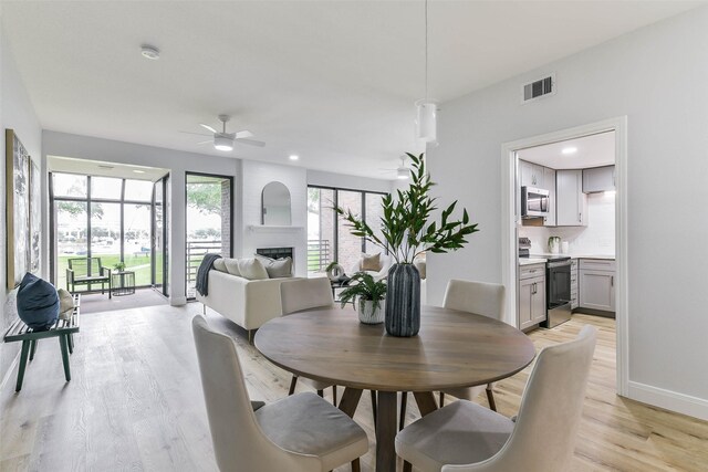 dining room featuring a fireplace, light hardwood / wood-style floors, and ceiling fan