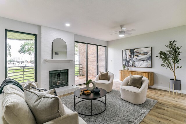 living room featuring light hardwood / wood-style flooring, a wealth of natural light, a fireplace, and ceiling fan