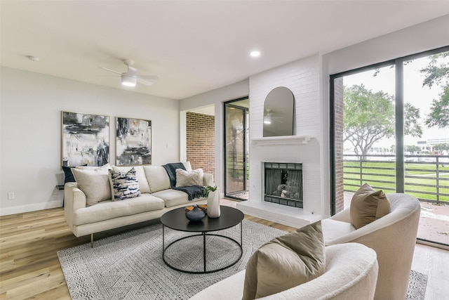 living room featuring light hardwood / wood-style flooring, a brick fireplace, and ceiling fan