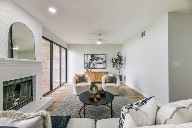 living room with a fireplace, light wood-type flooring, and ceiling fan