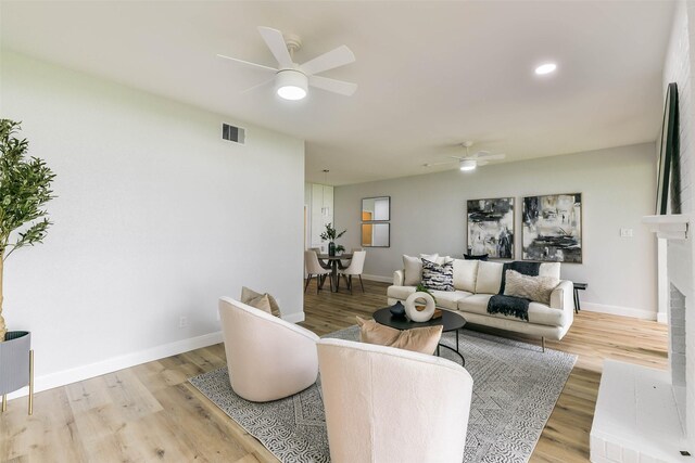 living room featuring a fireplace, ceiling fan, and light hardwood / wood-style floors