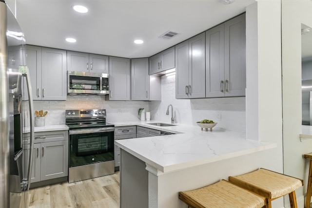 kitchen with light wood-type flooring, kitchen peninsula, appliances with stainless steel finishes, decorative backsplash, and sink