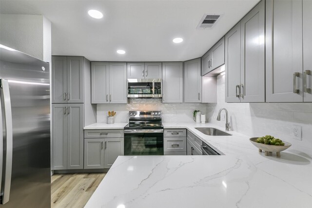 kitchen with light wood-type flooring, light stone counters, gray cabinets, appliances with stainless steel finishes, and sink