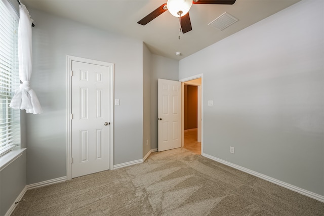 unfurnished bedroom with multiple windows, light colored carpet, and ceiling fan