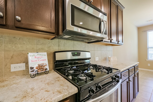 kitchen with tasteful backsplash, dark brown cabinets, gas range oven, and light stone countertops