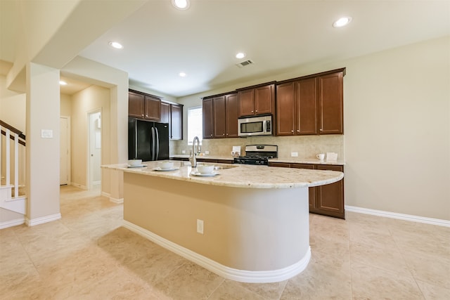 kitchen featuring light stone countertops, an island with sink, appliances with stainless steel finishes, and sink