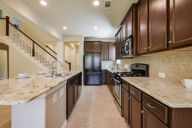 kitchen featuring sink, dark brown cabinets, black appliances, light stone countertops, and a center island with sink