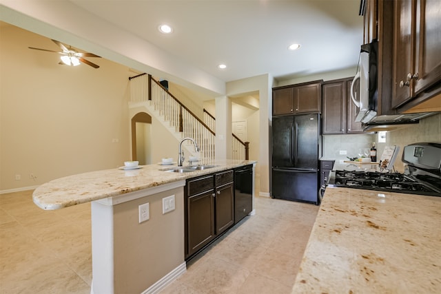 kitchen with light stone counters, sink, black appliances, and a center island with sink