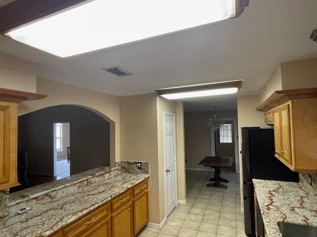 kitchen with a chandelier, black refrigerator, light stone countertops, and light tile patterned floors