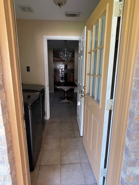 hallway with an inviting chandelier, washing machine and dryer, and light tile patterned flooring