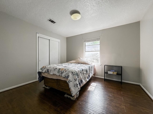 bedroom featuring visible vents, baseboards, wood finished floors, a textured ceiling, and a closet