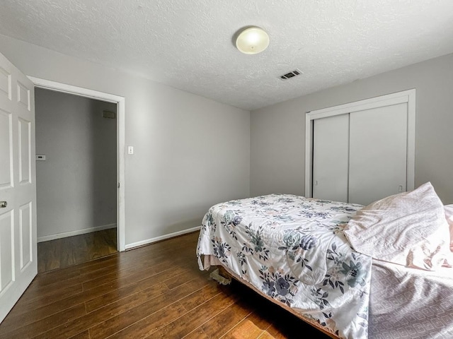 bedroom with a textured ceiling, wood finished floors, visible vents, baseboards, and a closet