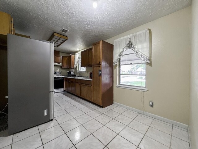 kitchen featuring sink, white appliances, light tile patterned floors, and a textured ceiling