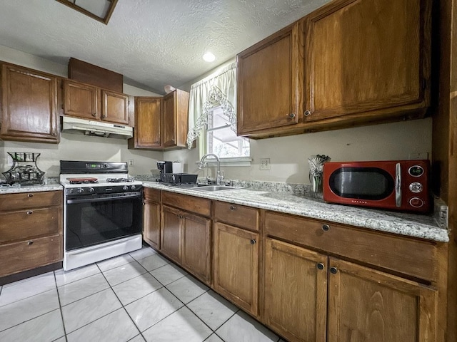 kitchen with vaulted ceiling, a textured ceiling, under cabinet range hood, a sink, and gas stove