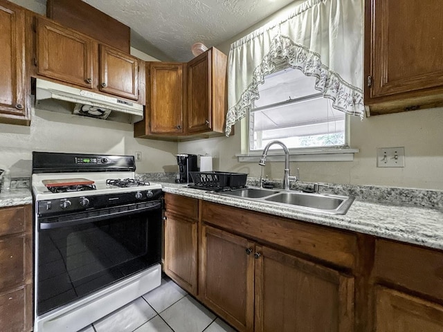 kitchen featuring range with gas stovetop, light countertops, a sink, and under cabinet range hood