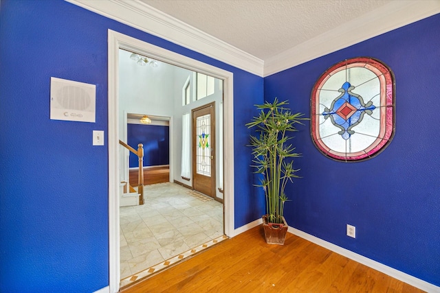 foyer entrance with ornamental molding, a textured ceiling, wood finished floors, baseboards, and stairs