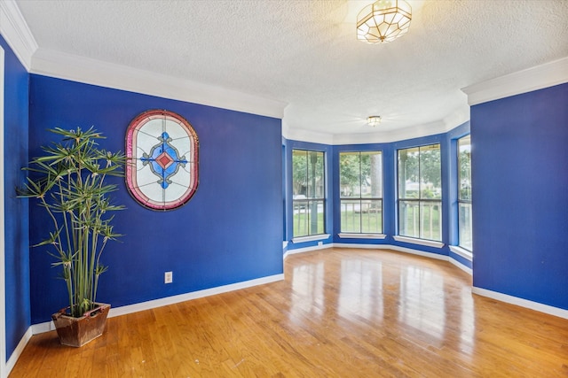 empty room with crown molding, a textured ceiling, wood finished floors, and baseboards