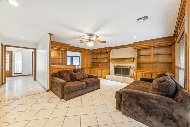 tiled living room featuring built in shelves, ceiling fan, and a large fireplace