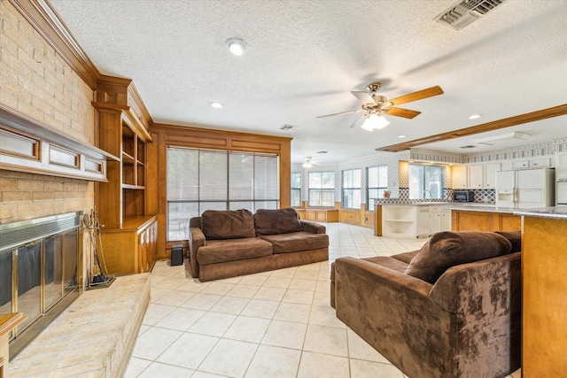 living room featuring visible vents, a textured ceiling, crown molding, a fireplace, and light tile patterned flooring