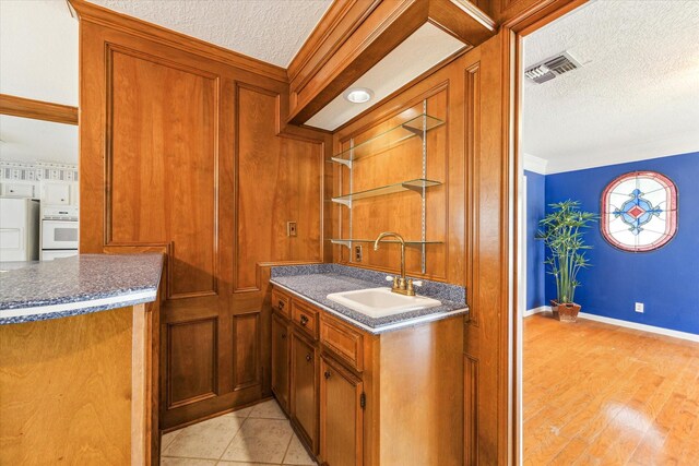 kitchen with crown molding, light wood-type flooring, white appliances, sink, and a textured ceiling