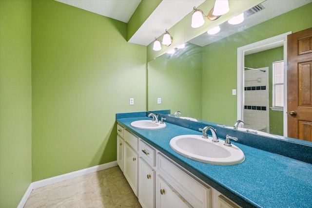 bathroom with double vanity, baseboards, a tile shower, and a sink