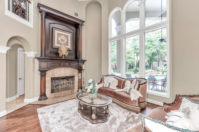 living room featuring wood-type flooring, a tiled fireplace, ornate columns, and plenty of natural light