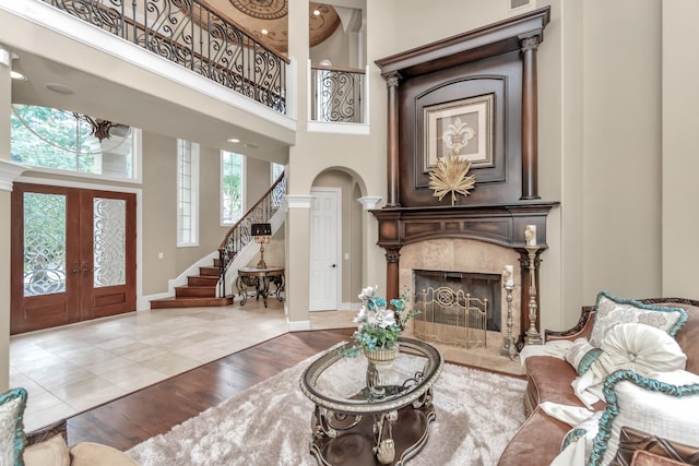 living room featuring wood-type flooring, french doors, a towering ceiling, and a high end fireplace