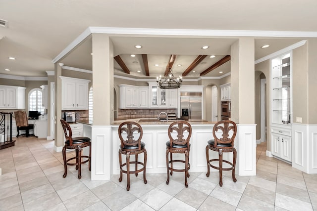 kitchen with beamed ceiling, tasteful backsplash, stainless steel appliances, light tile patterned floors, and white cabinetry