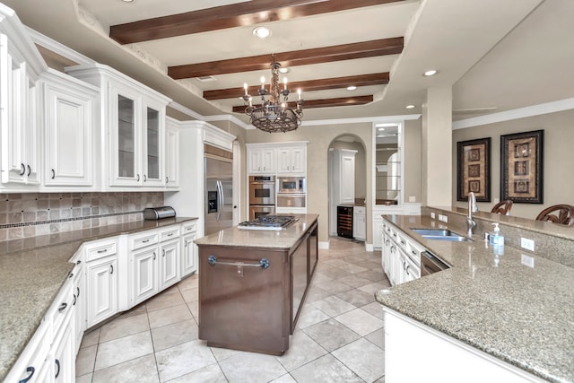 kitchen featuring built in appliances, ornamental molding, light stone countertops, a kitchen island, and backsplash