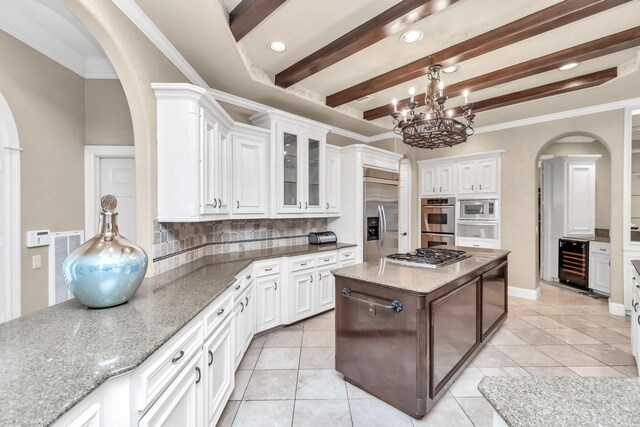 kitchen featuring built in appliances, backsplash, crown molding, white cabinetry, and beverage cooler