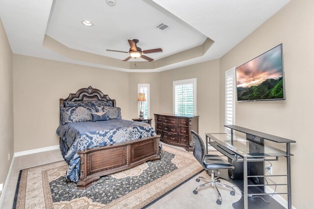 bedroom featuring ceiling fan, light hardwood / wood-style floors, and a tray ceiling